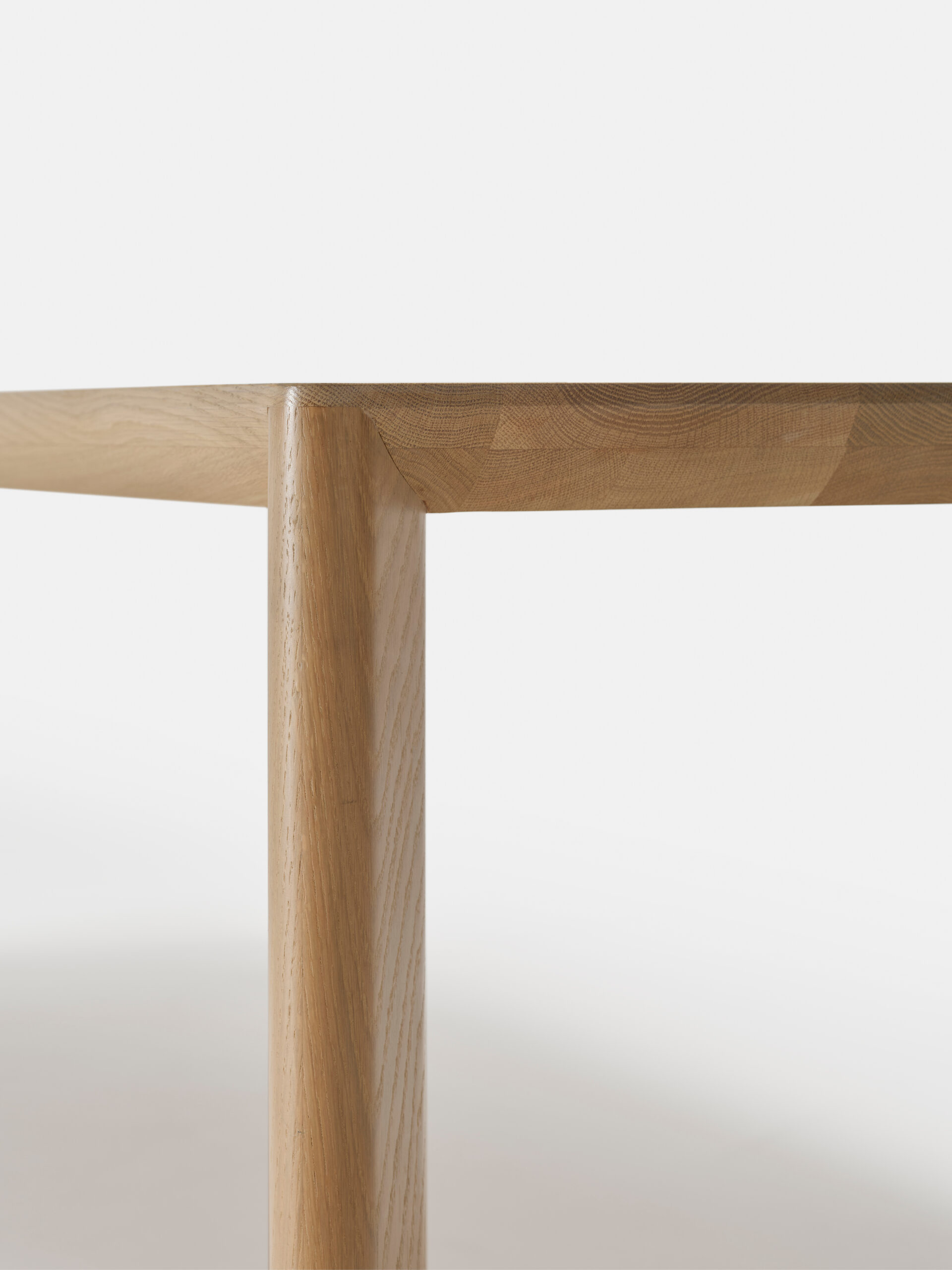 Close-up of a wooden table corner showing smooth, light wood grain, with a sharp angle between the tabletop and the leg against a plain white background.