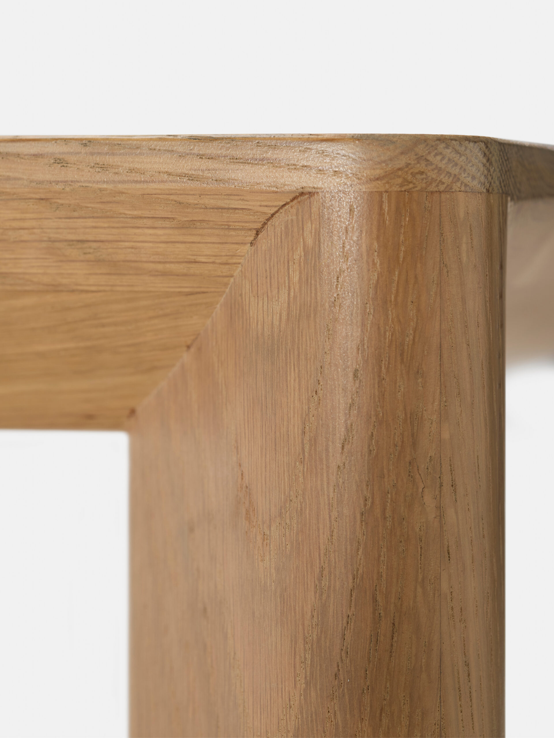 Close-up of a wooden table corner showing smooth, polished wood grain with clean, precise joinery and rounded edges against a plain white background.