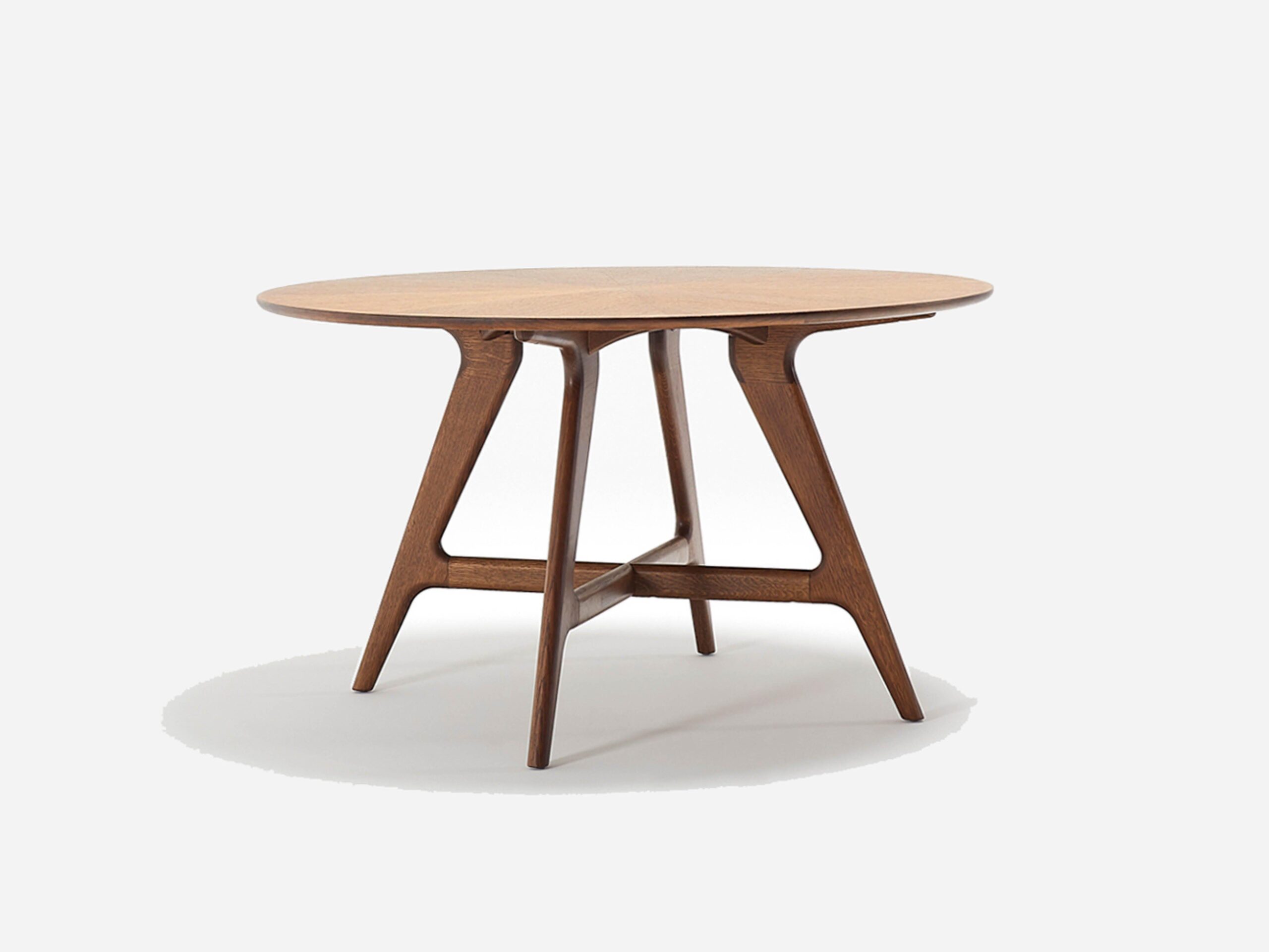 A round wooden table with a smooth top and angled legs joined by crossbars, set against a plain white background.