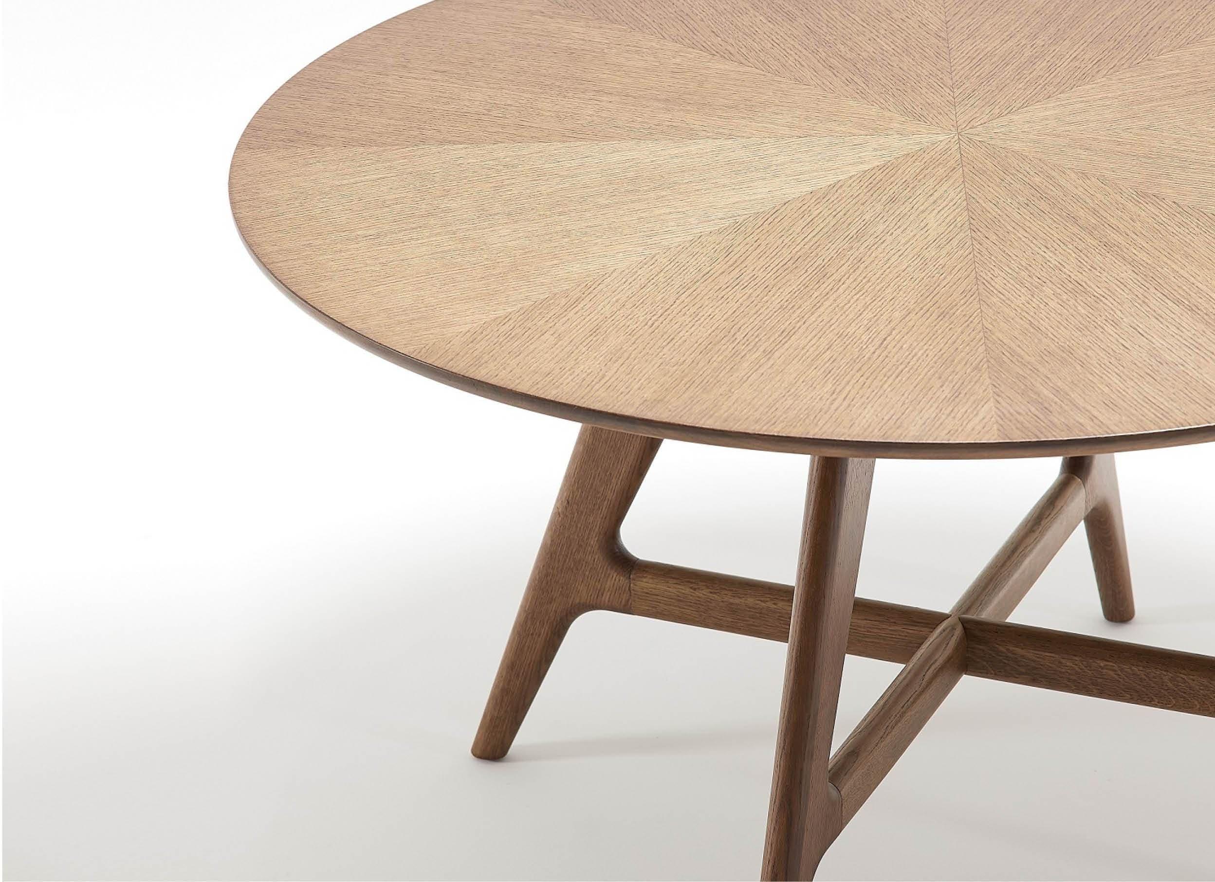A close-up of a round wooden table with a sunburst pattern on the tabletop and angled legs, set against a white background.