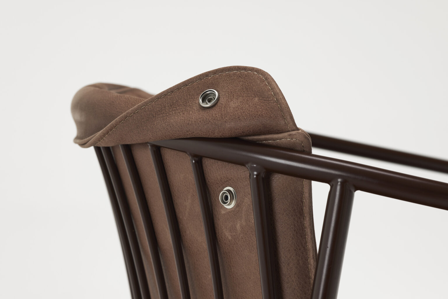 Close-up of the upper part of a chair backrest with brown leather upholstery, perfect for pairing with dining tables. The upholstery is secured with snap buttons to a black metal frame featuring multiple vertical rods. The leather has a smooth texture, and stitching details are visible. The background is white.