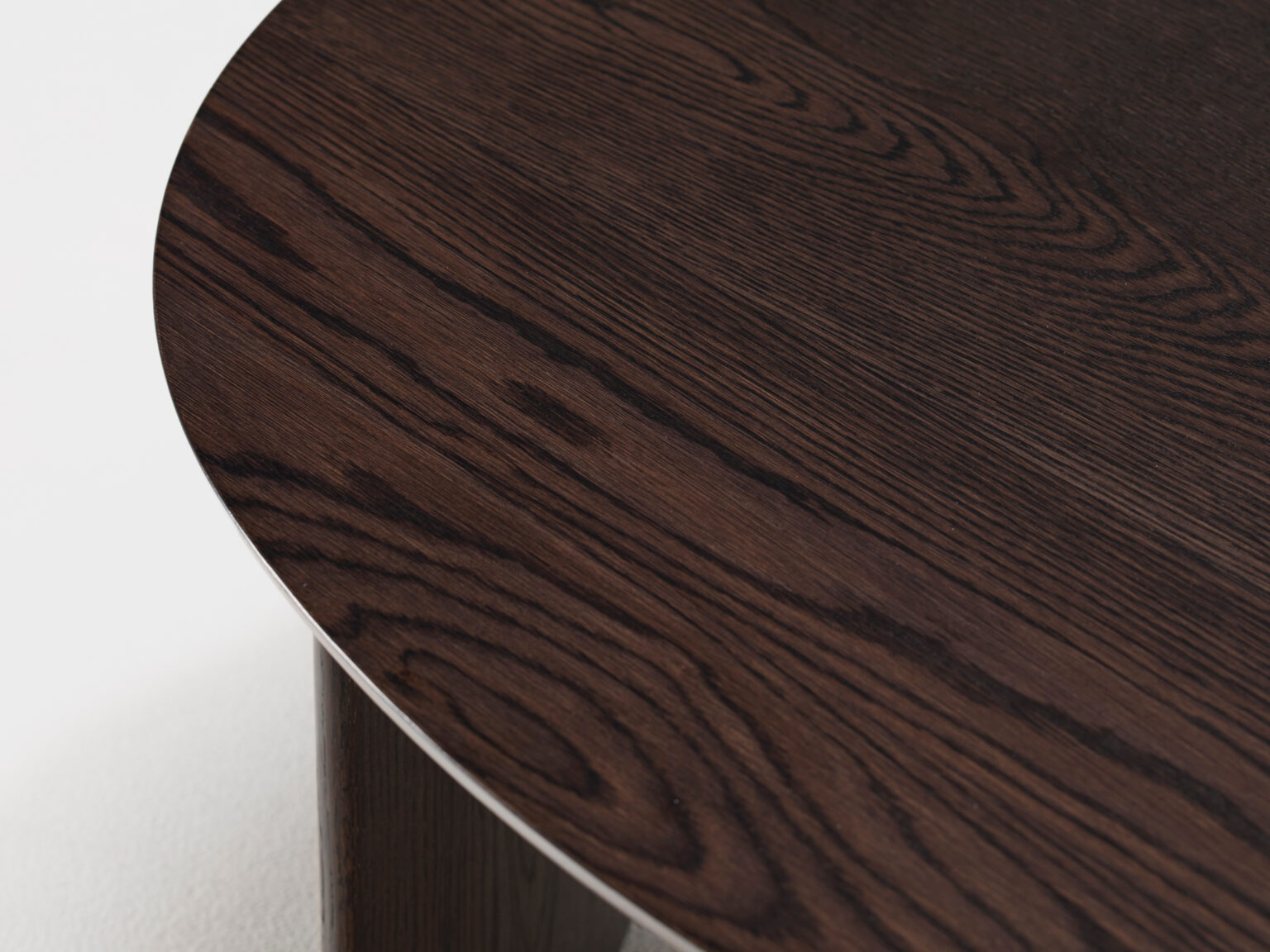 Close-up of a modern, dark wooden table with a smooth, rounded edge. The wood grain is visible, showcasing a rich pattern of lines and swirls. The table surface has a polished finish, highlighting the natural texture and color variations of the wood.