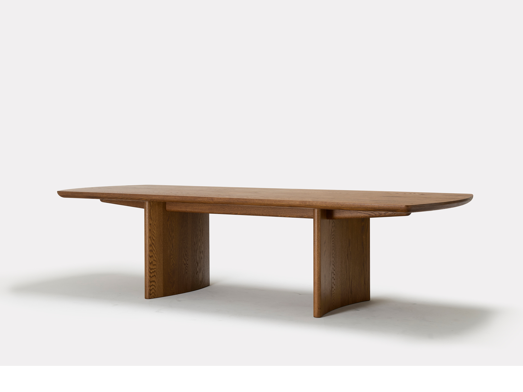 A modern wooden dining table with a smooth, rectangular top and two thick, curved legs as supports, set against a plain white background.