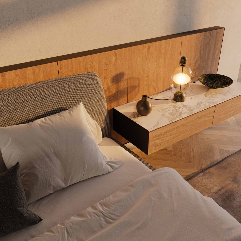 A modern bedroom with a headboard and a wooden nightstand. The bed has gray and white bedding. A glowing lamp, a small vase, and a bowl are on the nightstand with a marble top. The room features herringbone wood flooring.