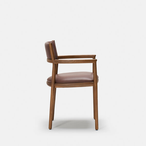 A wooden chair with a brown leather seat and backrest, shown in profile against a plain white background. The chair has armrests and simple, clean lines in its design.