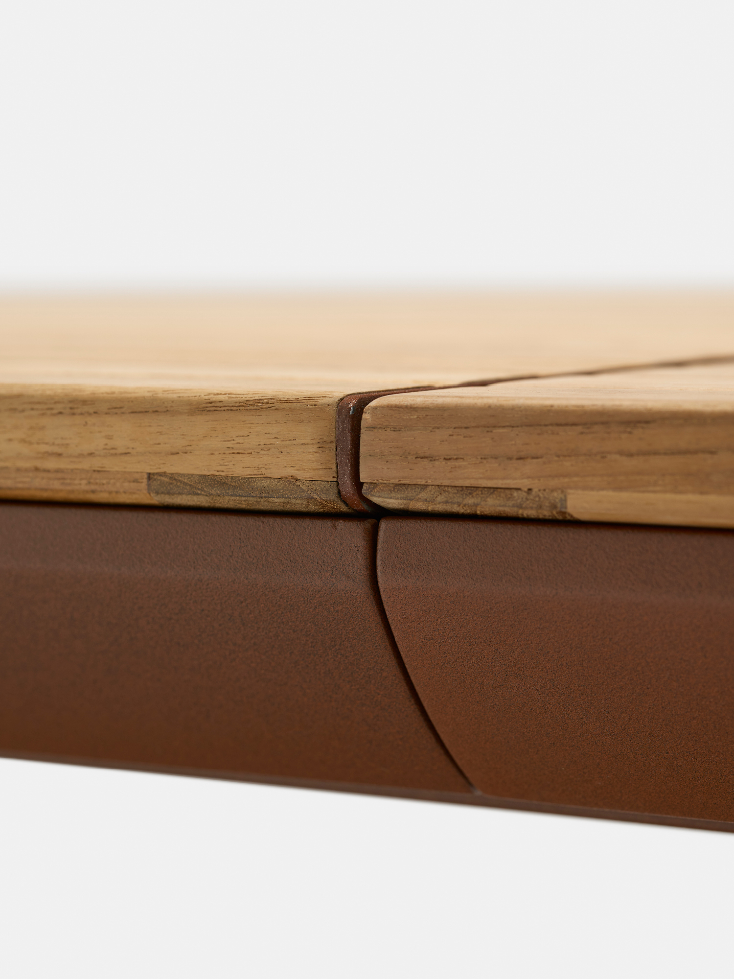 Close-up of the edge of a wooden tabletop with a precise joint, set on a brown metal frame, showing clean lines and craftsmanship against a plain light background.