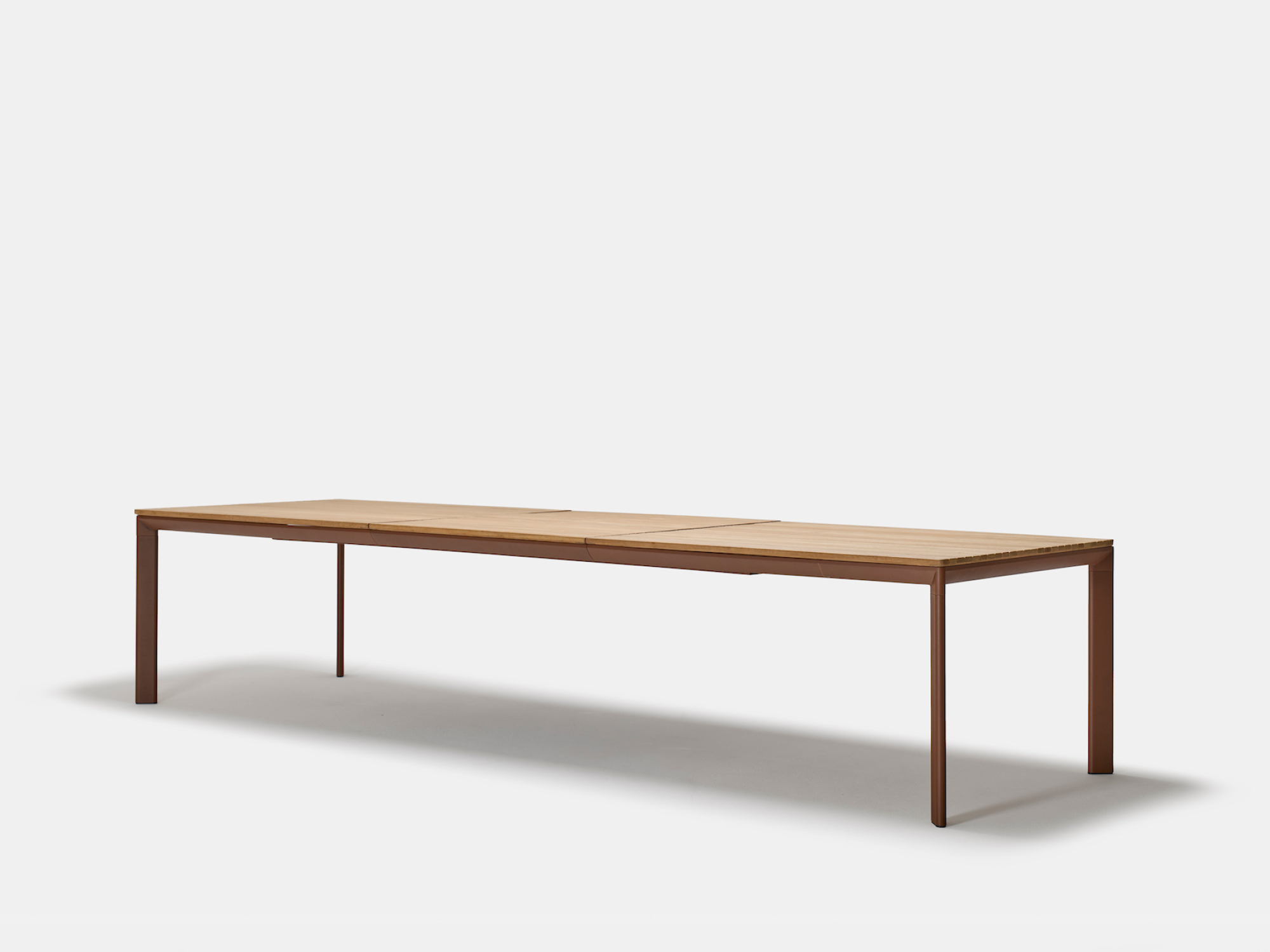 A long, rectangular wooden table with clean lines and slim legs, set against a plain white background. The table has a minimalist, modern design.