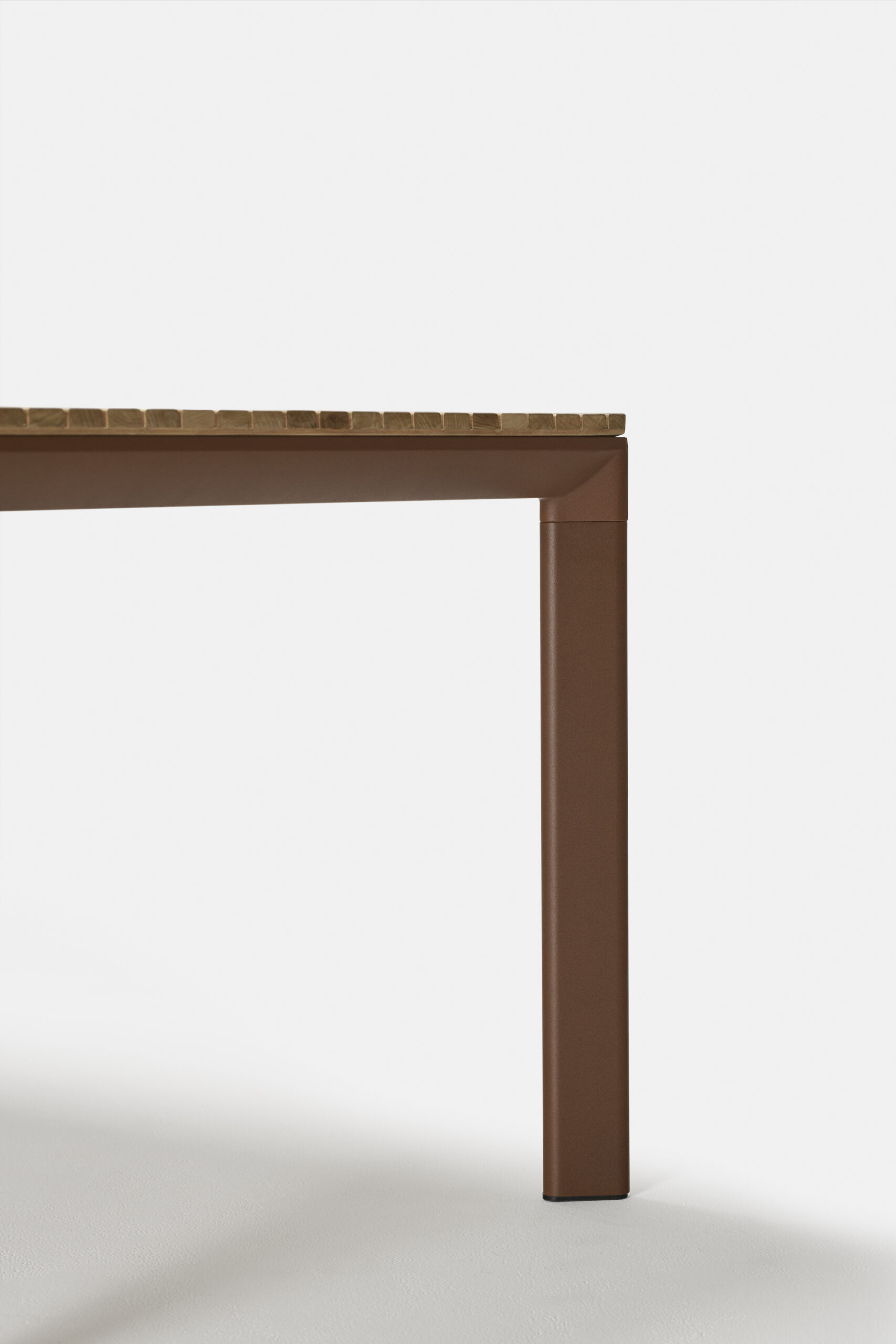 Close-up of the corner of a modern table with a light brown wooden top and a thick, rectangular brown leg against a plain white background.