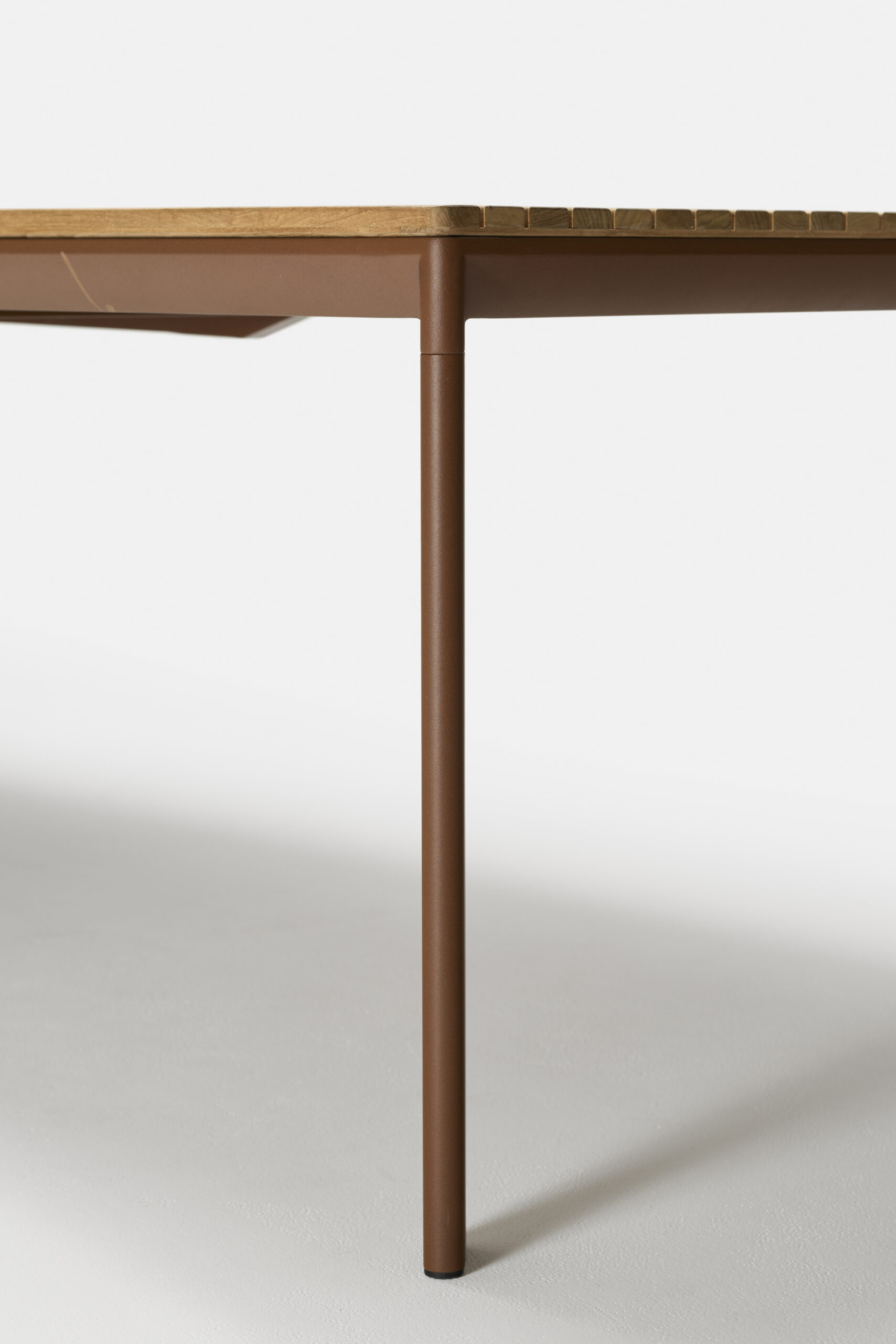 A close-up view of the corner of a modern table with a wooden top and a brown metal leg, set against a plain white background.