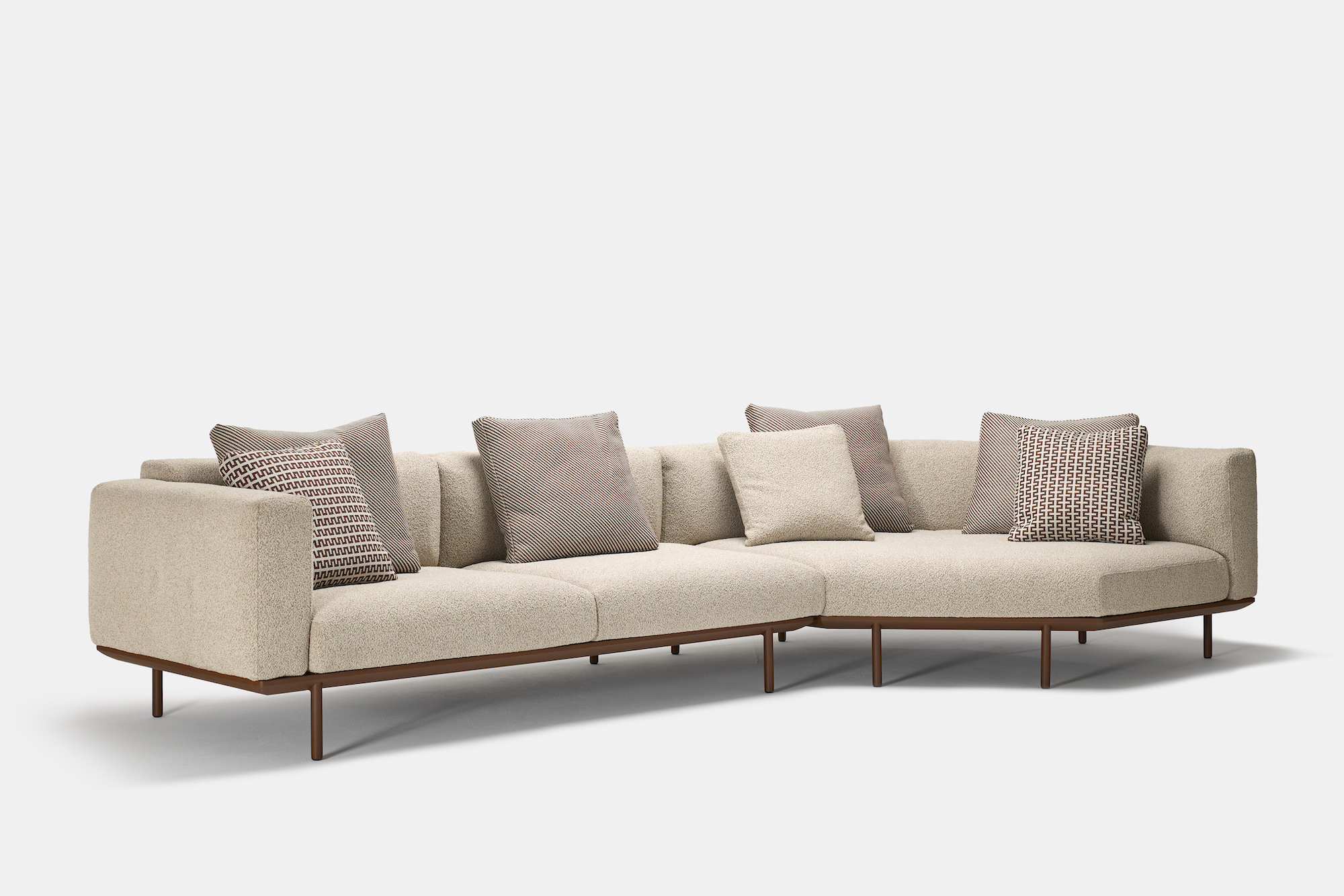 A modern L-shaped beige sectional sofa with brown metal legs, featuring several patterned and plain throw pillows, set against a plain white background.