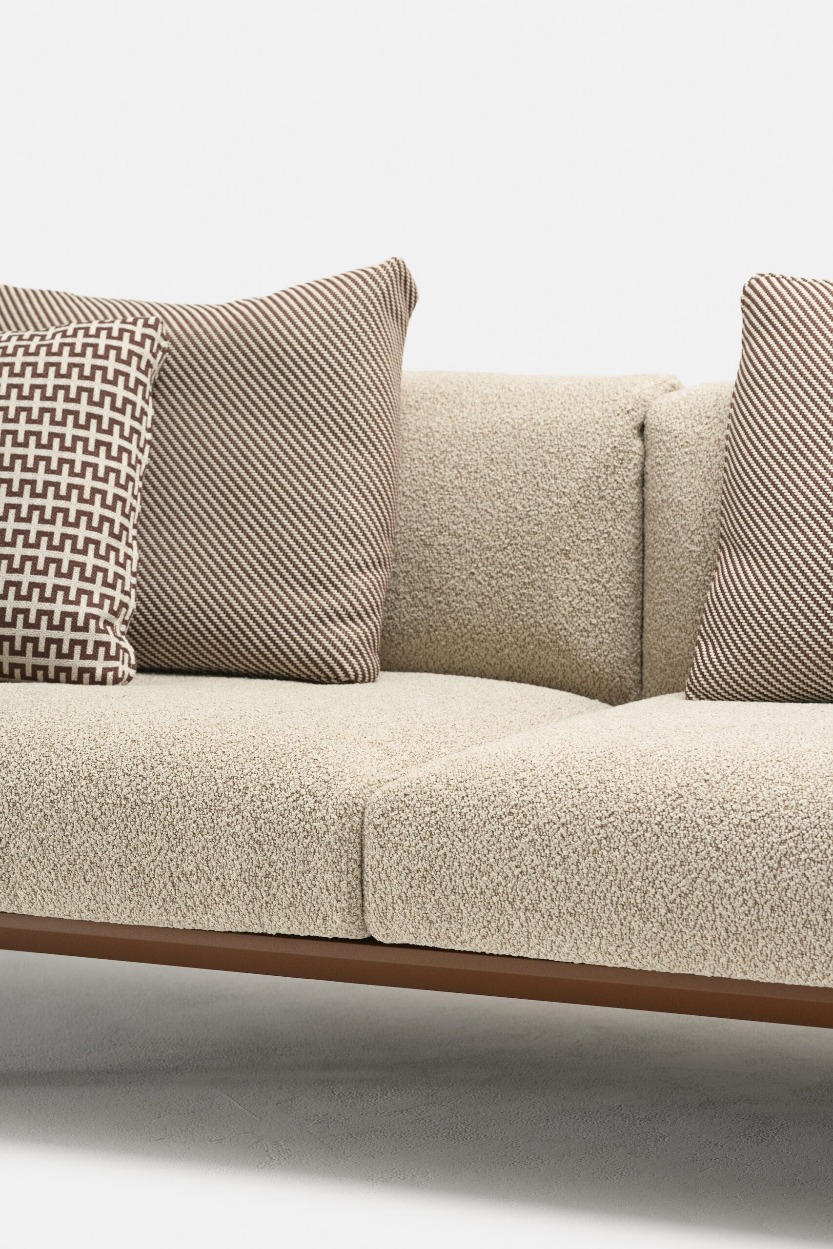 A beige textured sofa with a wooden base, featuring two large brown-striped pillows and one smaller pillow with a geometric brown and white pattern. The background is plain white.