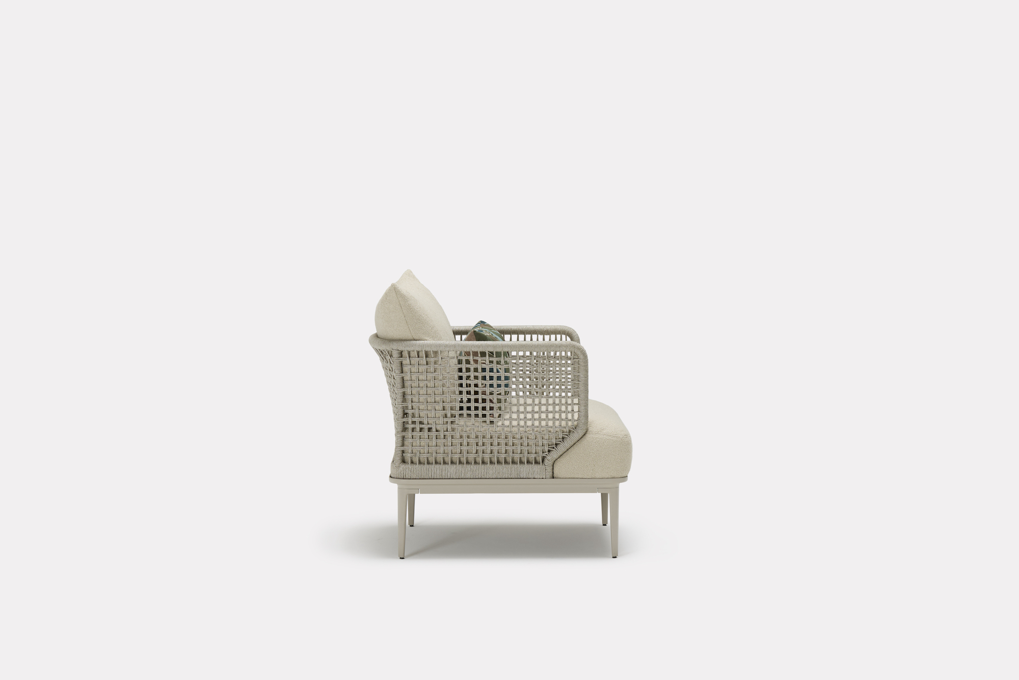 Side view of a modern beige armchair with woven back and sides, cushioned seat and backrest, and a green accent pillow, set against a plain white background.
