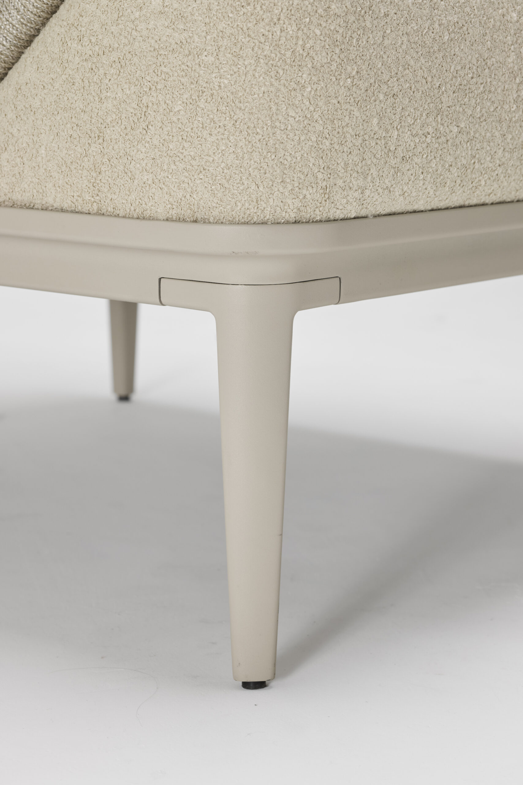 Close-up of the bottom corner of a beige upholstered chair with smooth, light-colored metal legs on a white background.