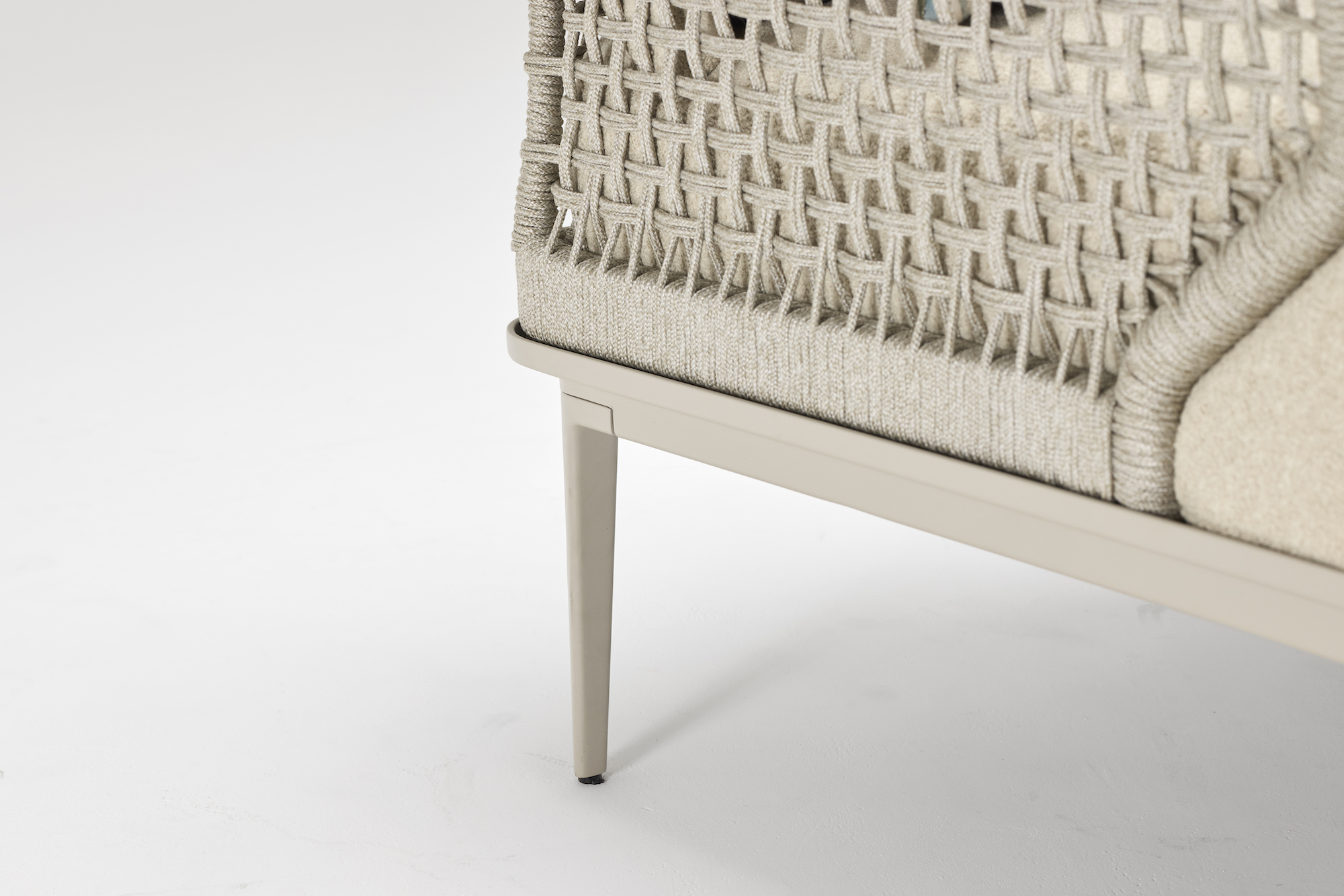 Close-up of a modern chair leg with a beige metal finish, textured woven side panel, and light-colored upholstered cushion, set against a white background.