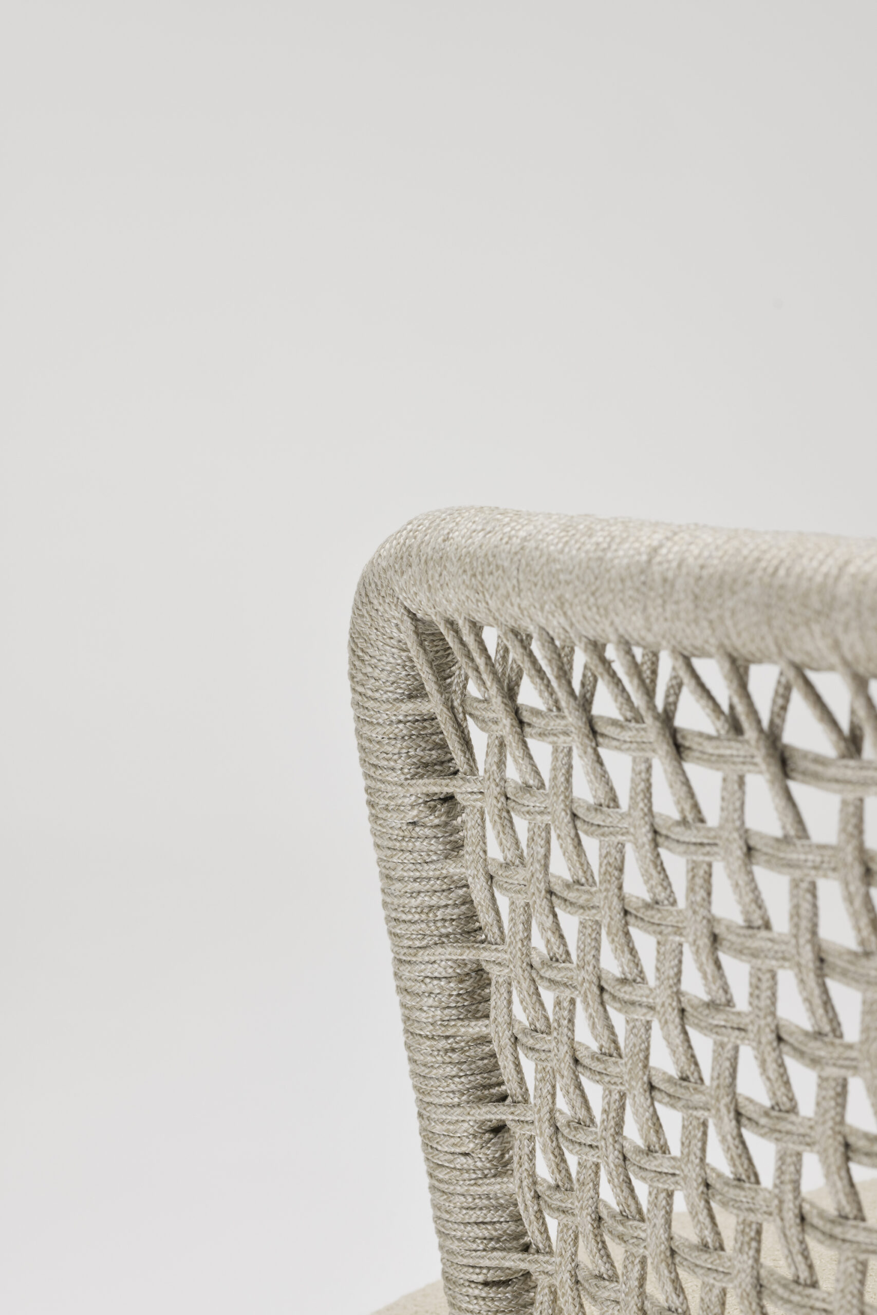 Close-up of the backrest of a beige woven chair, showing detailed textured rope or fiber weaving against a plain white background.