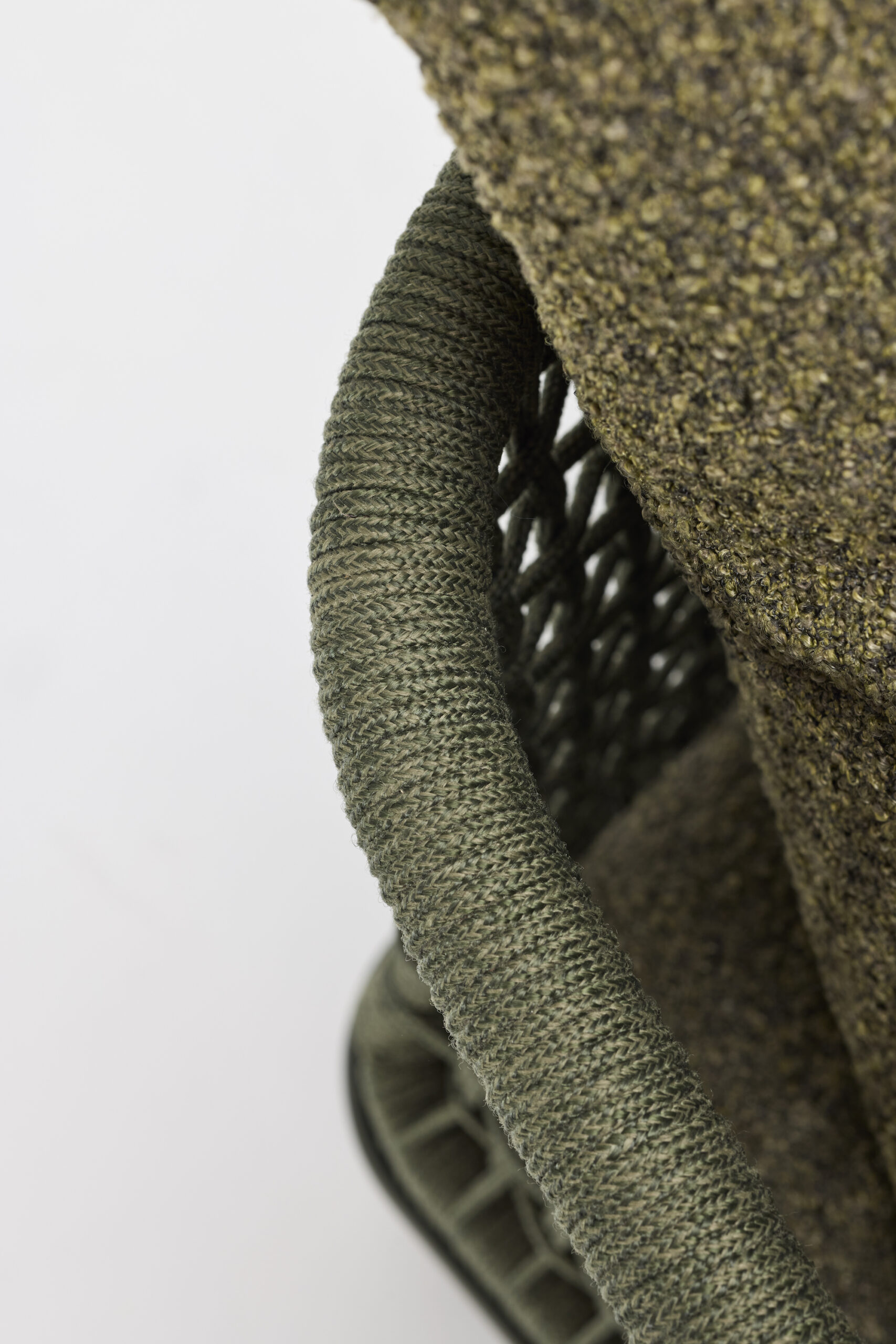 Close-up of a textured green chair with a woven frame and a matching speckled green cushion, set against a plain white background.