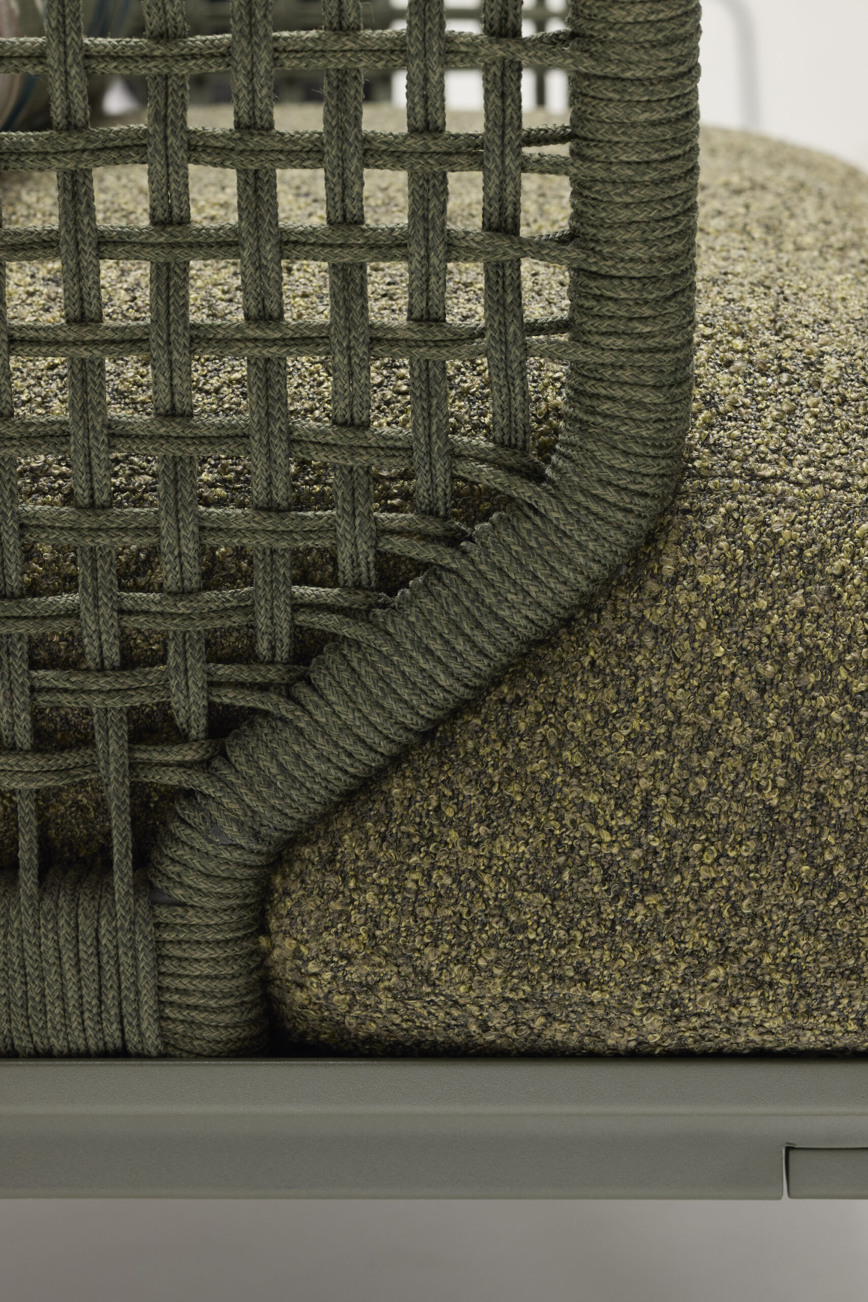 Close-up of a chair with a green woven rope backrest and armrest, and an olive-green textured cushion on a sturdy frame. The materials and craftsmanship are clearly visible.