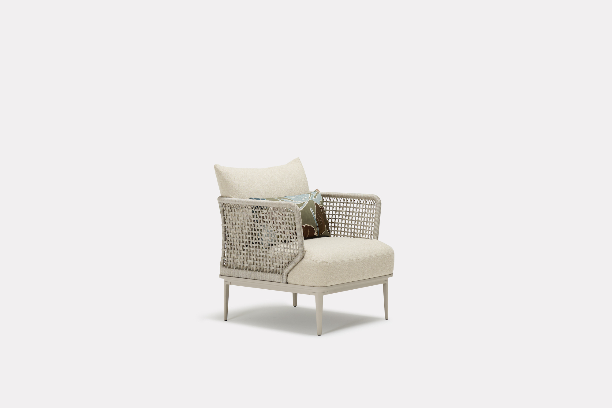 A modern beige armchair with woven sides, slim legs, and a cushioned seat, featuring two decorative throw pillows. The chair is set against a plain white background.