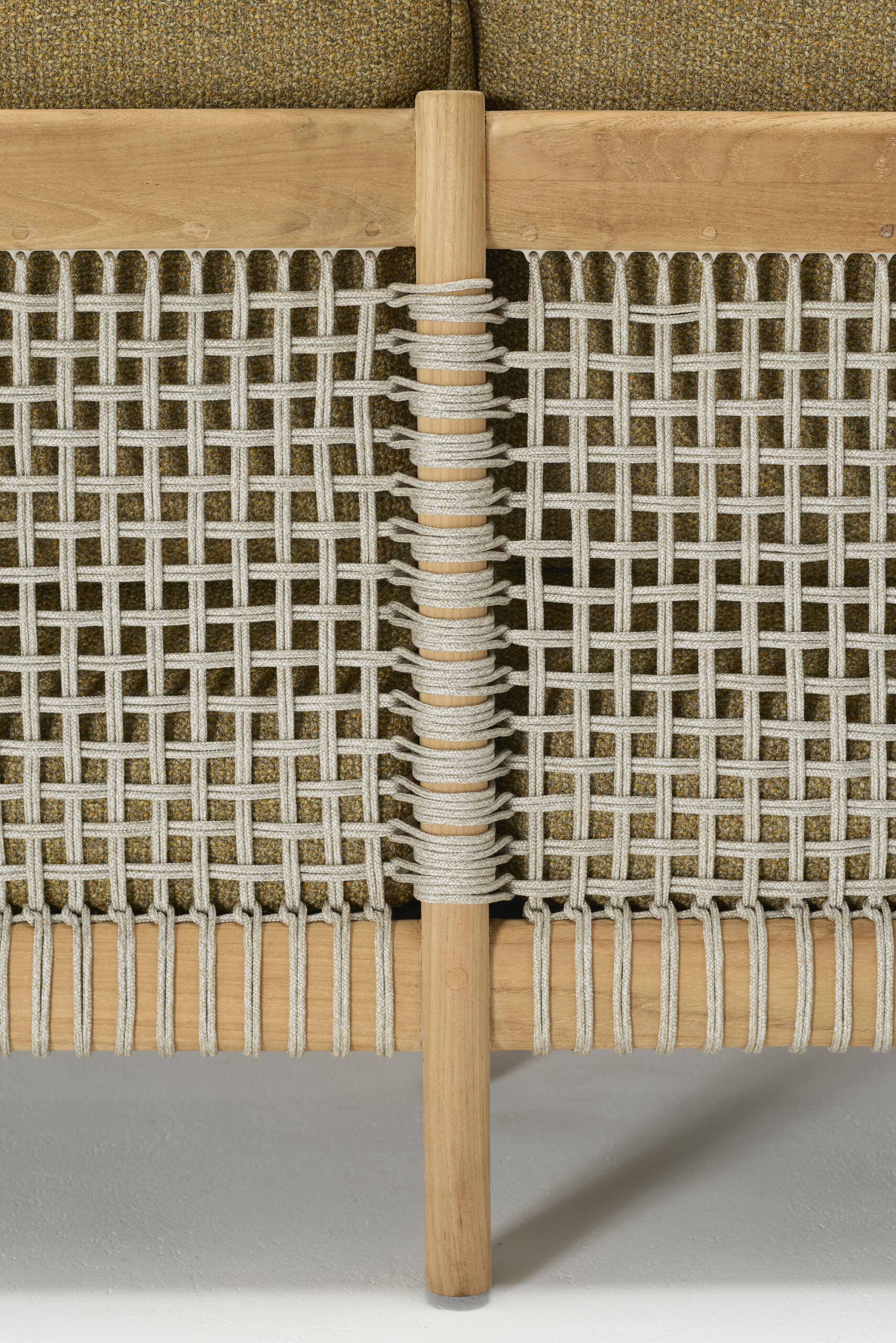 Close-up of a piece of furniture with a wooden frame, featuring beige woven rope detailing in a grid pattern and olive-green upholstered cushions in the background.