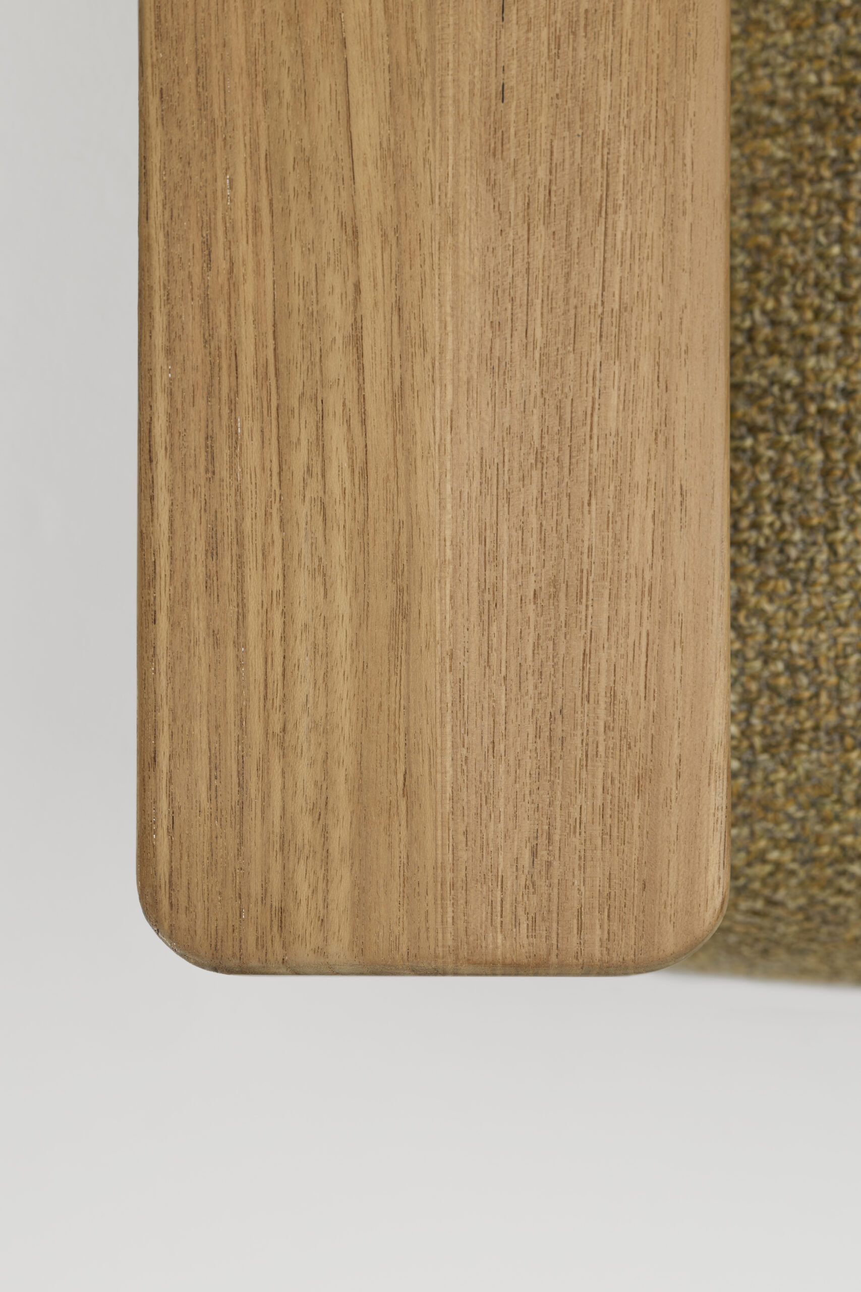 A close-up, top-down view of a wooden tabletop with rounded edges next to a textured, moss-green fabric surface.