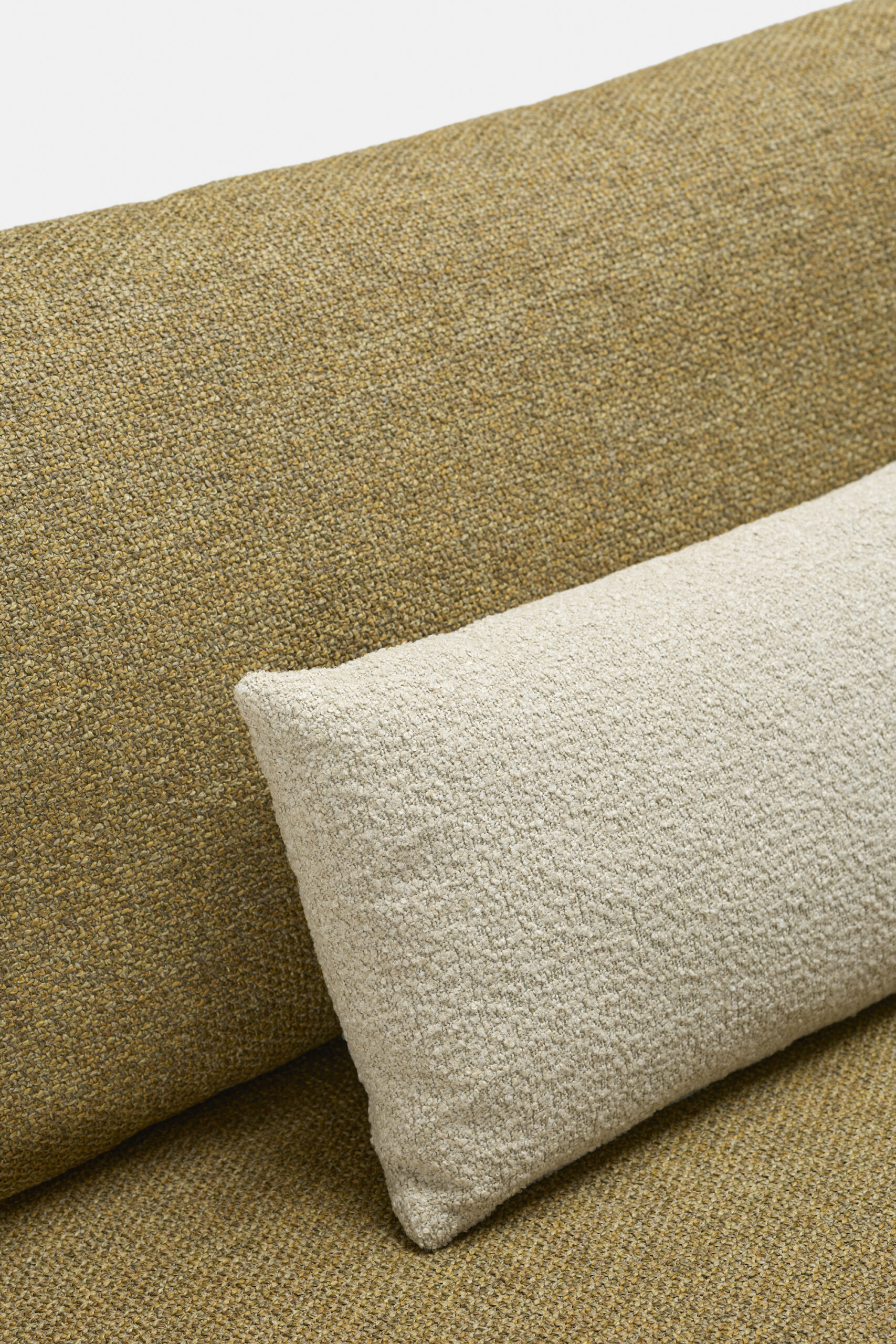Close-up of a textured mustard yellow sofa with a rectangular off-white pillow resting against the back cushion.