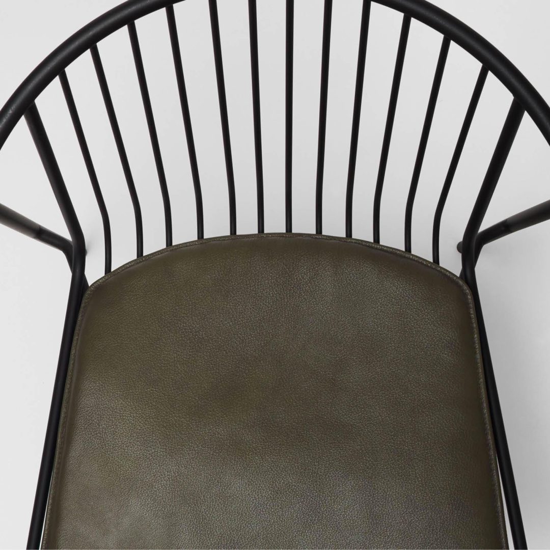 A close-up, top view of a modern chair with a black metal frame, vertical rod backrest, and a dark olive green cushioned seat against a white background.